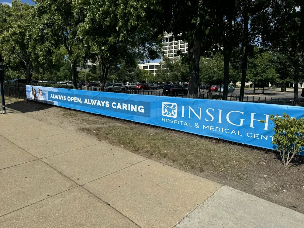 Large outdoor vinyl banner sign installed on fence for Insight Hospital in Chicago, IL